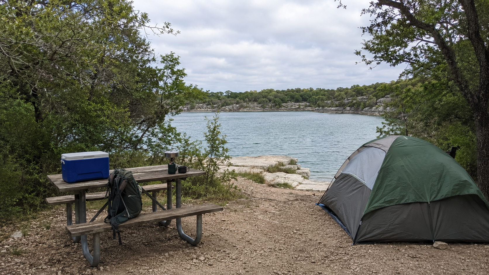 Tent, picnic table, cooler, and backpack at a wooded lakeside campsite in Texas.