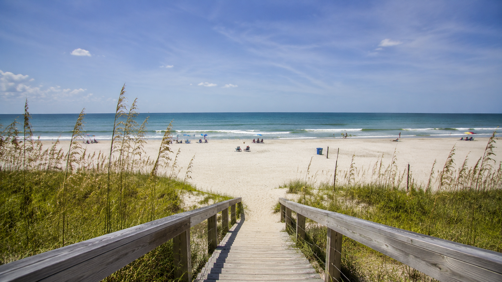 A sandy Texas Gulf Coast beach with rolling waves and beach grass beneath a blue sky.