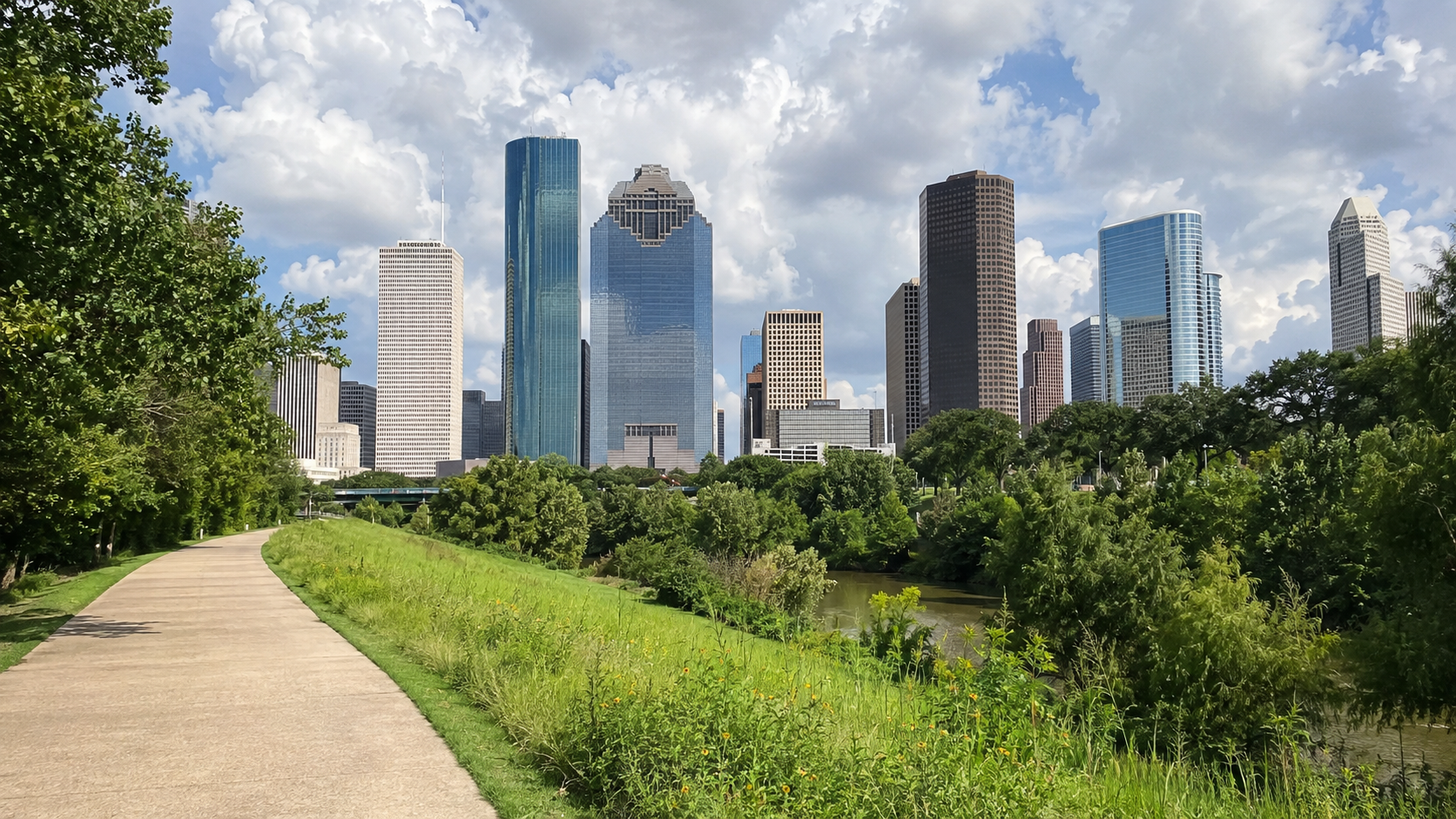 Downtown Houston skyline rising beyond a green park path and bayou.