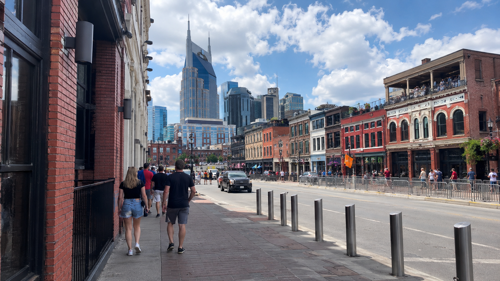 Pedestrians and historic brick buildings along Broadway with the Nashville skyline under a blue sky.